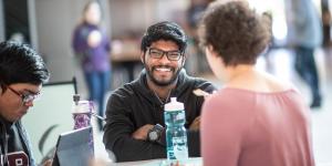 A student smiling while sitting at a lunch table with their friends